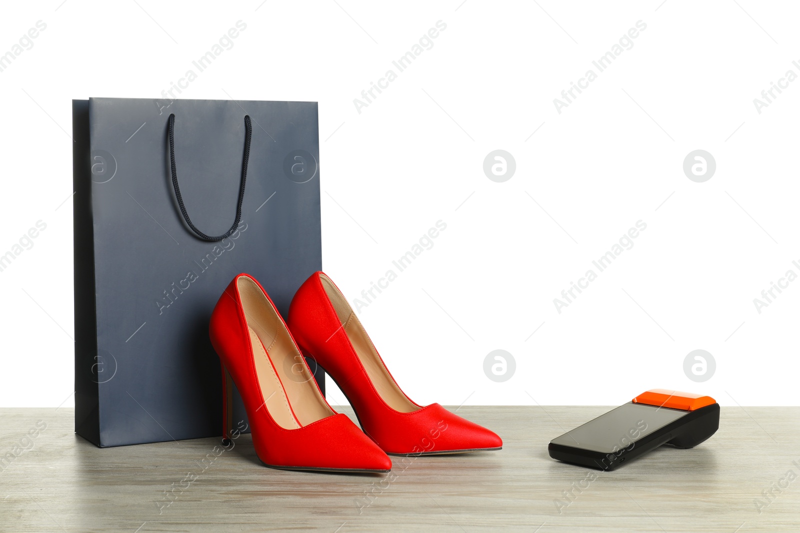 Photo of Payment terminal, shopping bag and high heeled shoes on wooden table against white background