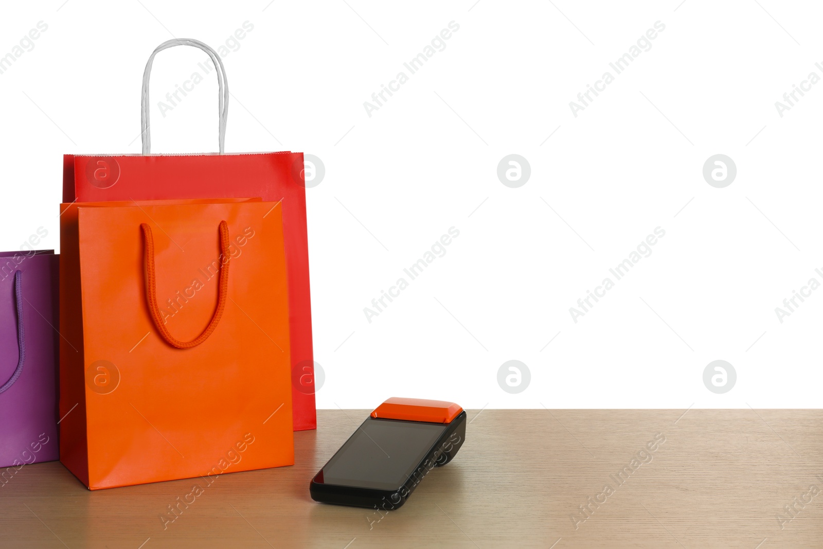 Photo of Payment terminal and shopping bags on wooden table against white background