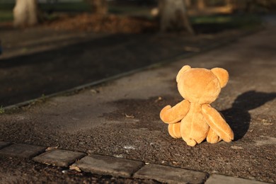 Photo of Lost brown teddy bear on ground outdoors, back view. Space for text