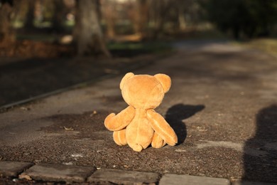 Photo of Lost brown teddy bear on ground outdoors, back view