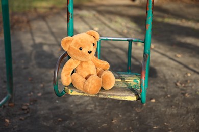 Photo of Lost brown teddy bear on swing outdoors