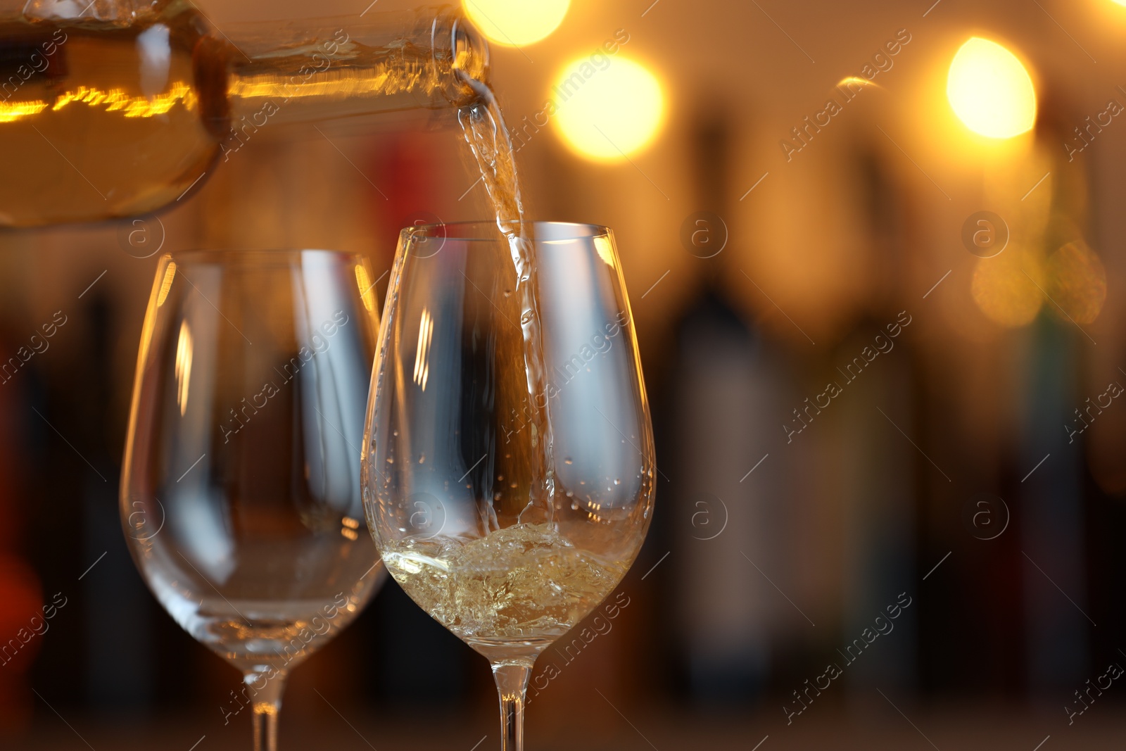 Photo of Pouring white wine into glass against blurred background with festive lights, closeup and space for text. Bokeh effect