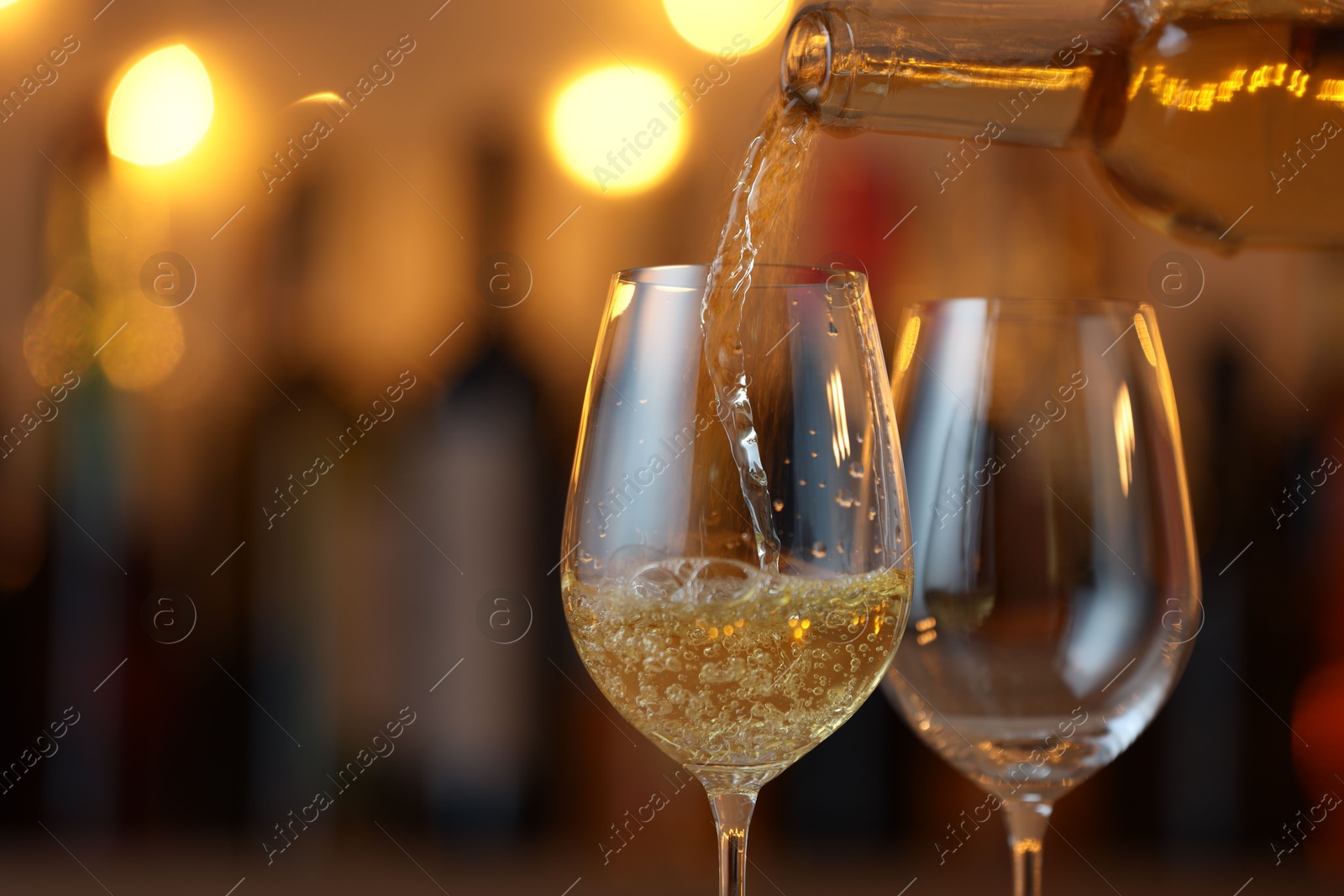 Photo of Pouring white wine into glass against blurred background with festive lights, closeup and space for text. Bokeh effect