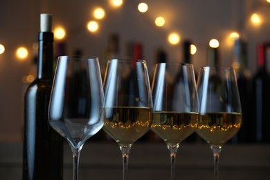 Photo of Tasty white wine in glasses against blurred background with festive lights, closeup. Bokeh effect