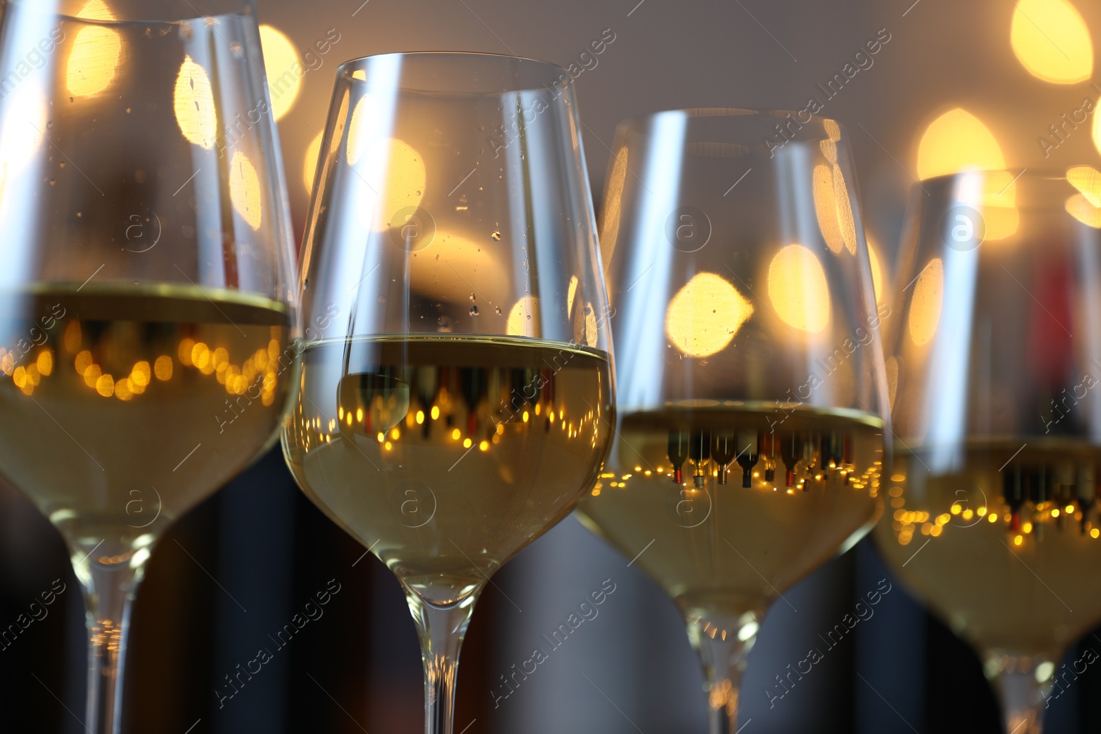 Photo of Tasty white wine in glasses against blurred background with festive lights, closeup. Bokeh effect