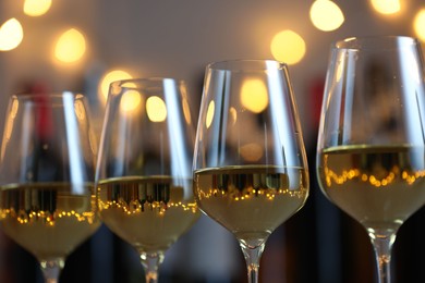 Photo of Tasty white wine in glasses against blurred background with festive lights, closeup. Bokeh effect