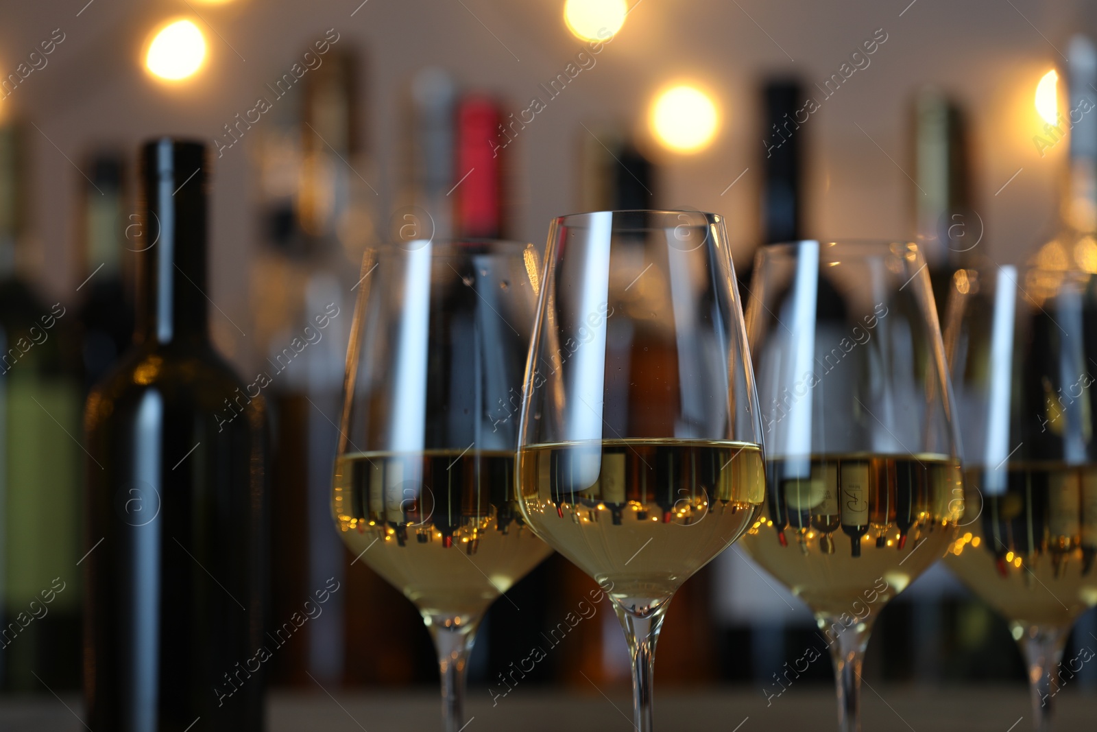 Photo of Tasty white wine in glasses against blurred background with festive lights, closeup. Bokeh effect