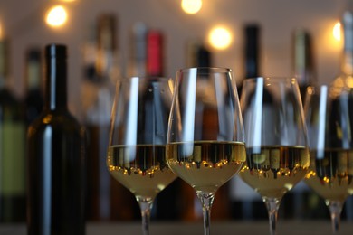 Photo of Tasty white wine in glasses against blurred background with festive lights, closeup. Bokeh effect