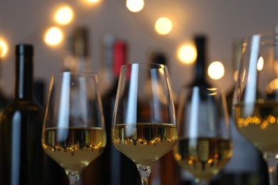 Photo of Tasty white wine in glasses against blurred background with festive lights, closeup. Bokeh effect