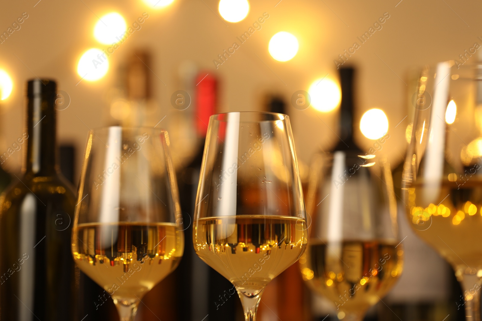 Photo of Tasty white wine in glasses against blurred background with festive lights, closeup. Bokeh effect