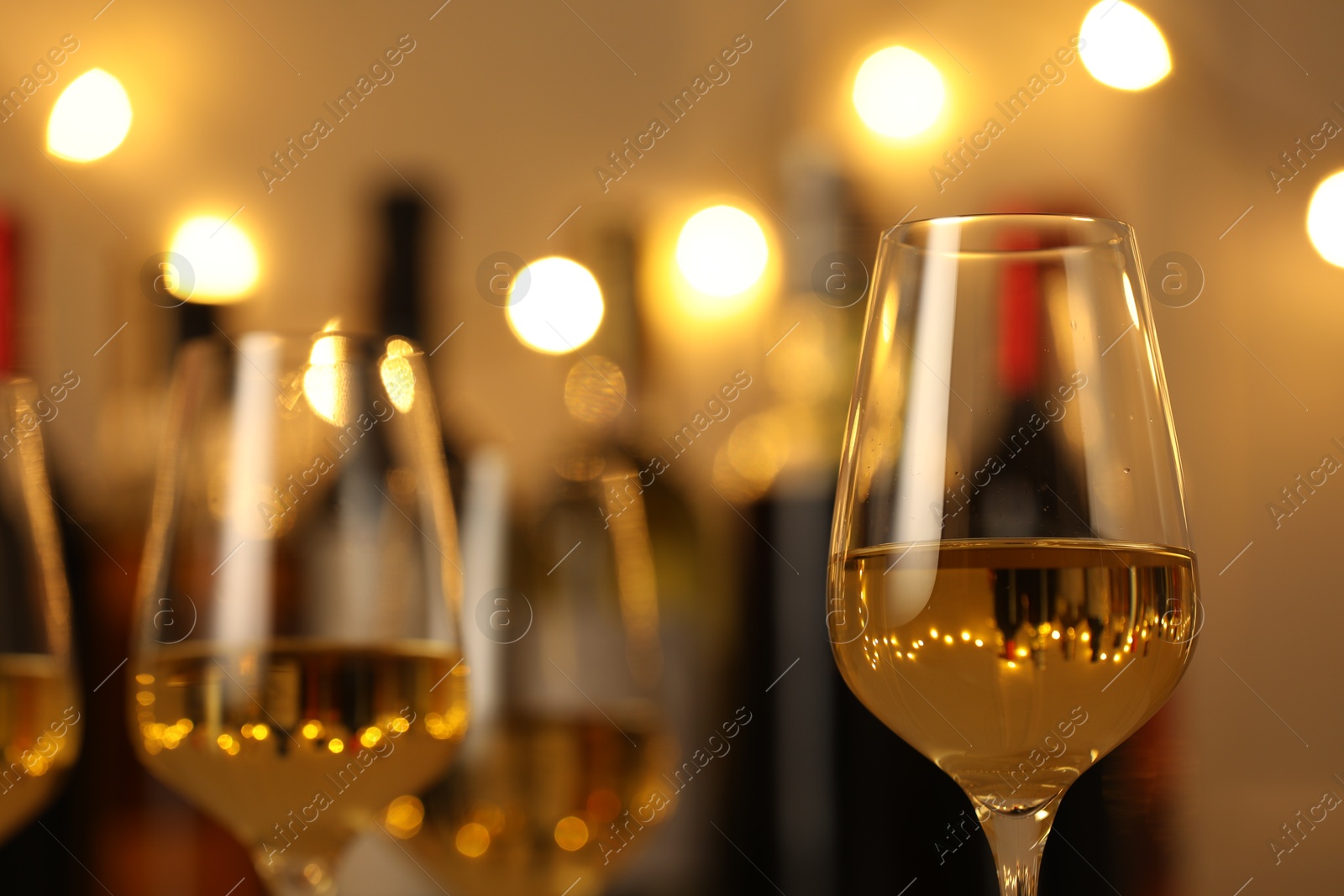 Photo of Tasty white wine in glasses against blurred background with festive lights, closeup. Bokeh effect