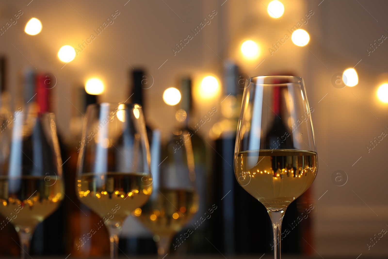 Photo of Tasty white wine in glasses against blurred background with festive lights, closeup. Bokeh effect