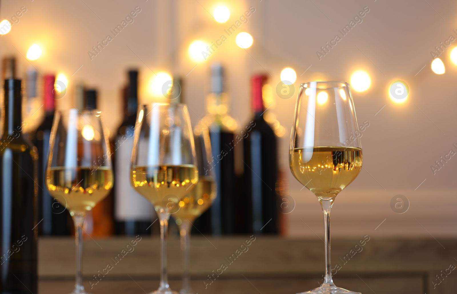 Photo of Tasty white wine in glasses against blurred background with festive lights. Bokeh effect