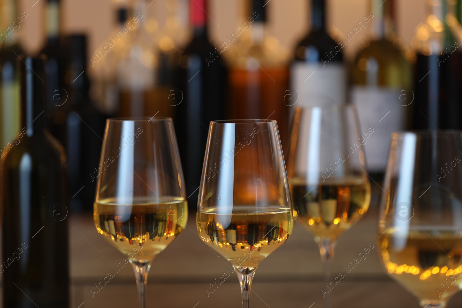 Photo of Tasty white wine in glasses against blurred background with festive lights, closeup. Bokeh effect