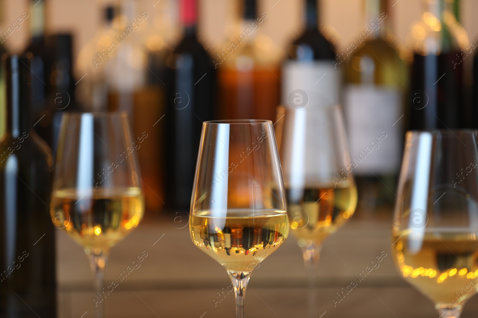 Photo of Tasty white wine in glasses against blurred background with festive lights, closeup. Bokeh effect