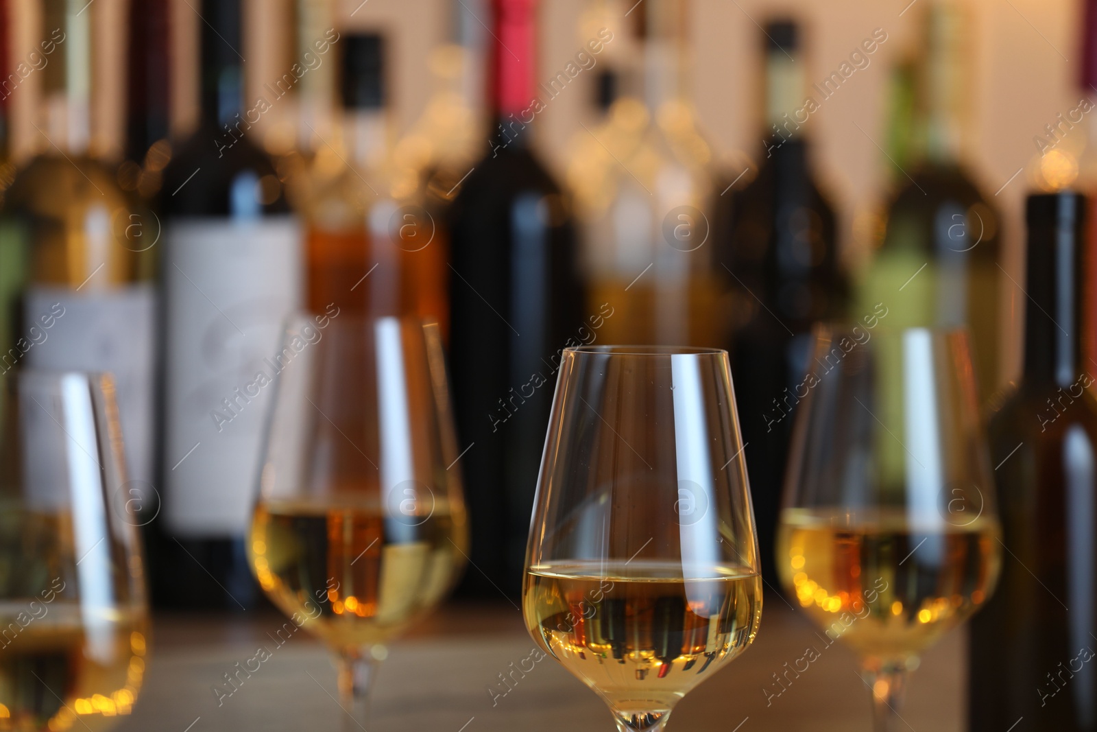 Photo of Tasty white wine in glasses against blurred background with festive lights, closeup. Bokeh effect