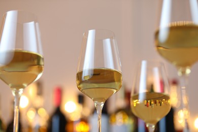 Photo of Tasty white wine in glasses against blurred background with festive lights, closeup. Bokeh effect