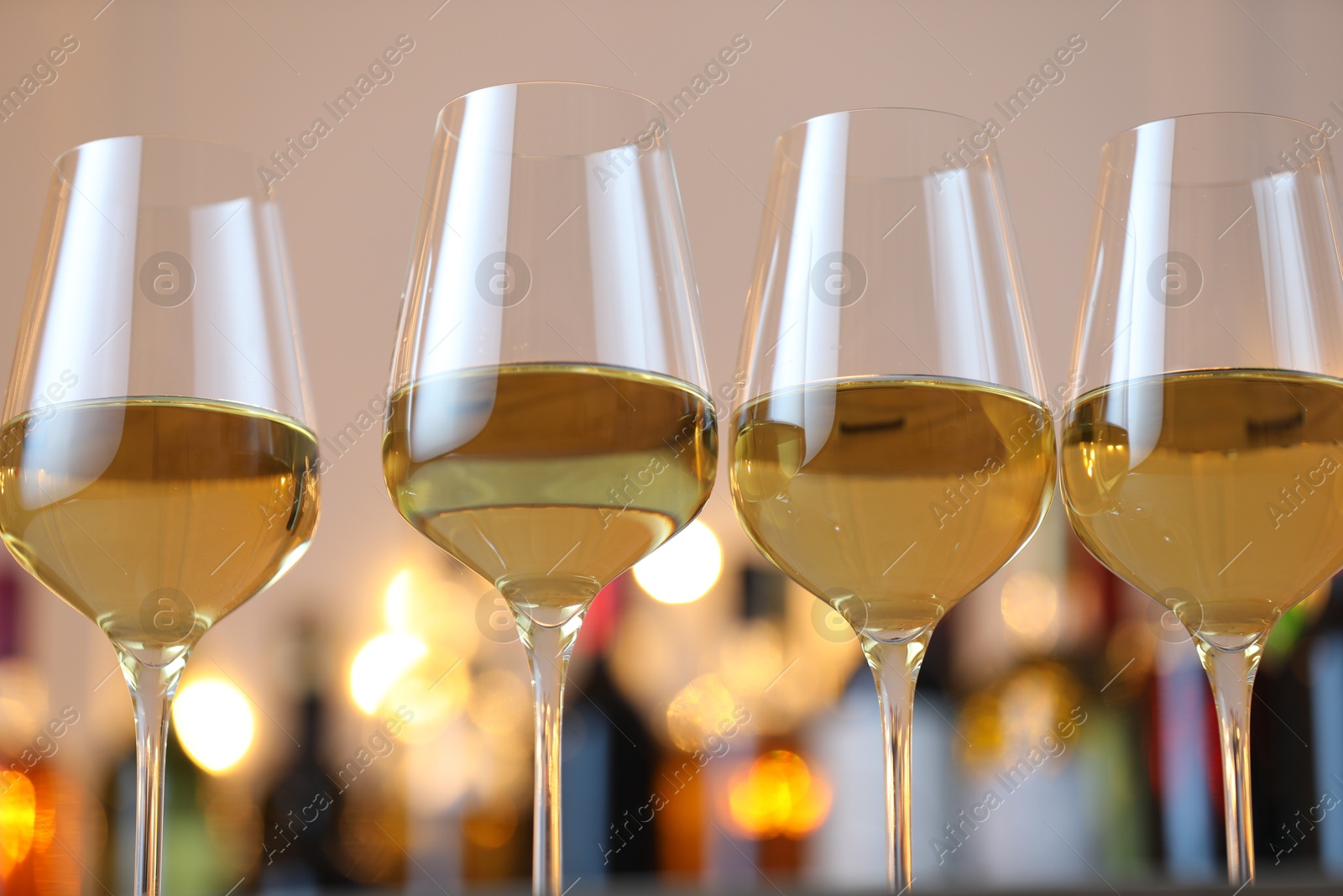 Photo of Tasty white wine in glasses against blurred background with festive lights, closeup. Bokeh effect