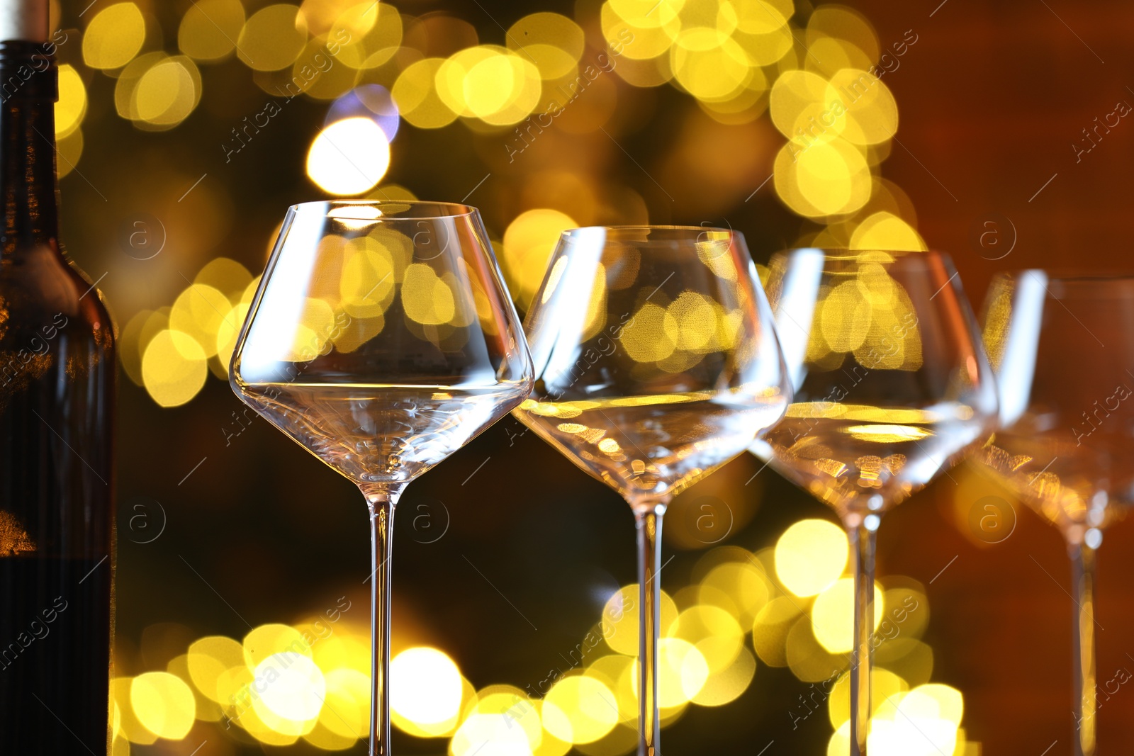 Photo of Wine glasses and bottle against blurred lights, closeup. Bokeh effect