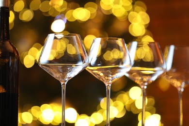 Photo of Wine glasses and bottle against blurred lights, closeup. Bokeh effect