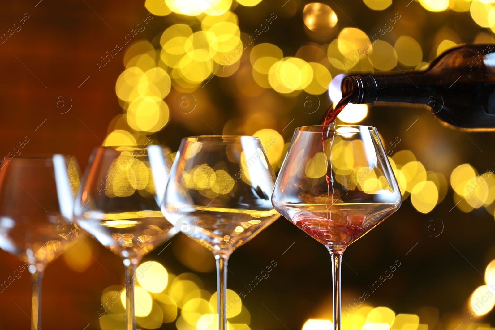 Photo of Pouring red wine into glass against blurred lights, closeup. Bokeh effect