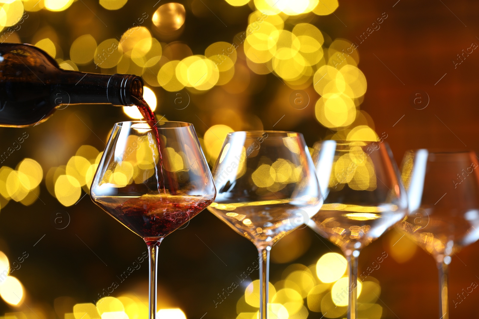 Photo of Pouring red wine into glass against blurred lights, closeup. Bokeh effect