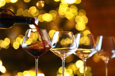 Photo of Pouring red wine into glass against blurred lights, closeup. Bokeh effect