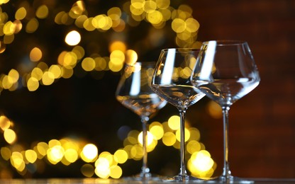 Photo of Wine glasses on table against blurred lights, space for text. Bokeh effect