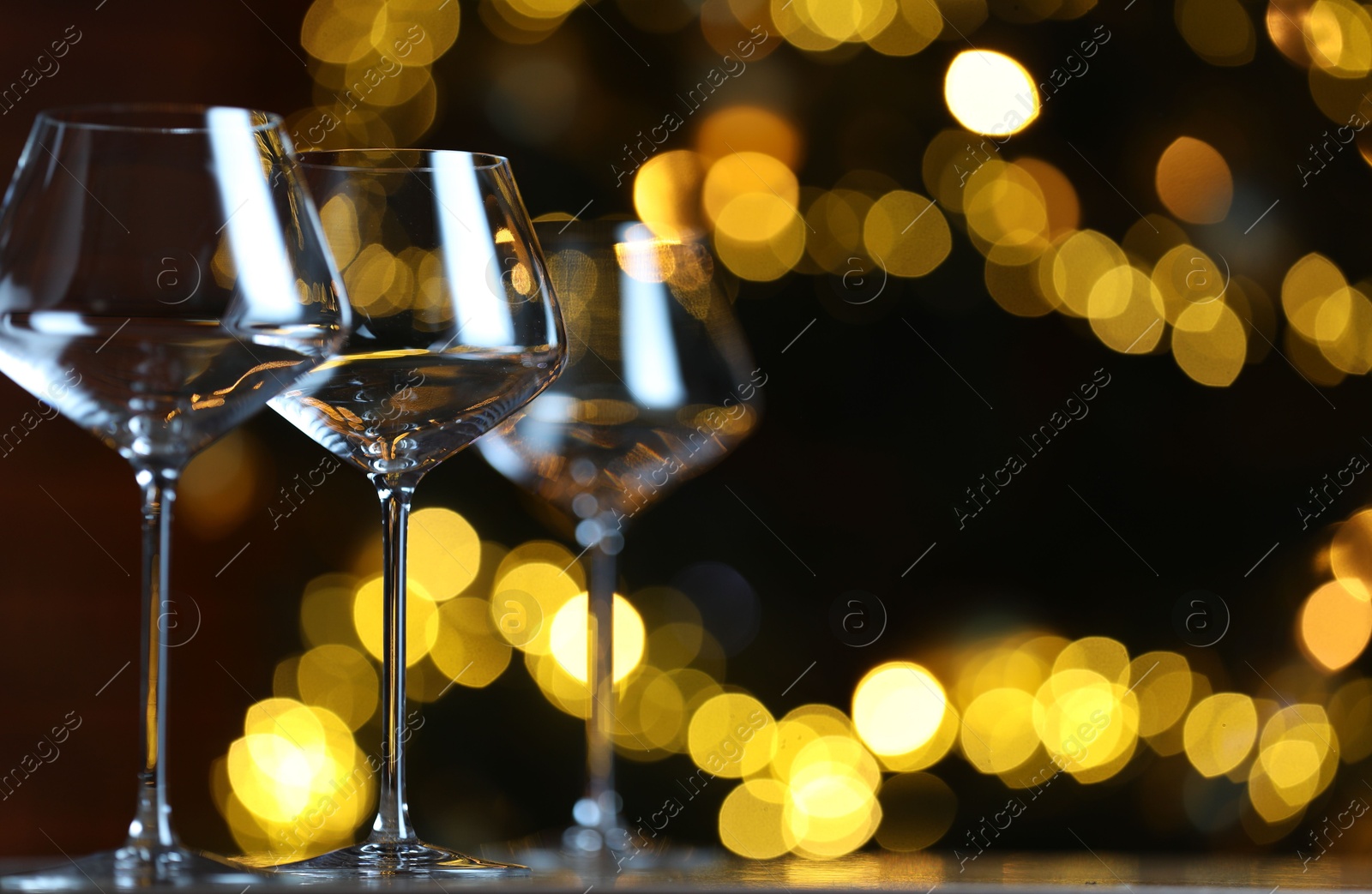 Photo of Wine glasses on table against blurred lights, space for text. Bokeh effect