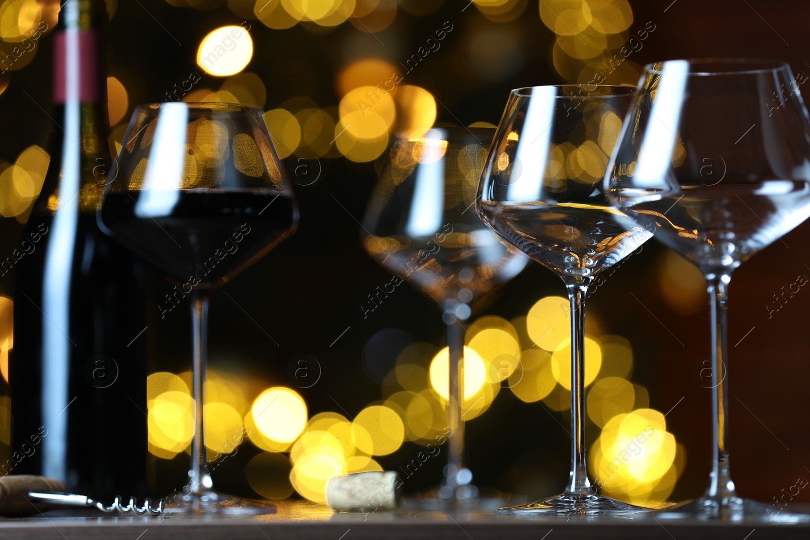 Photo of Glass with red wine and empty ones on table against blurred lights. Bokeh effect