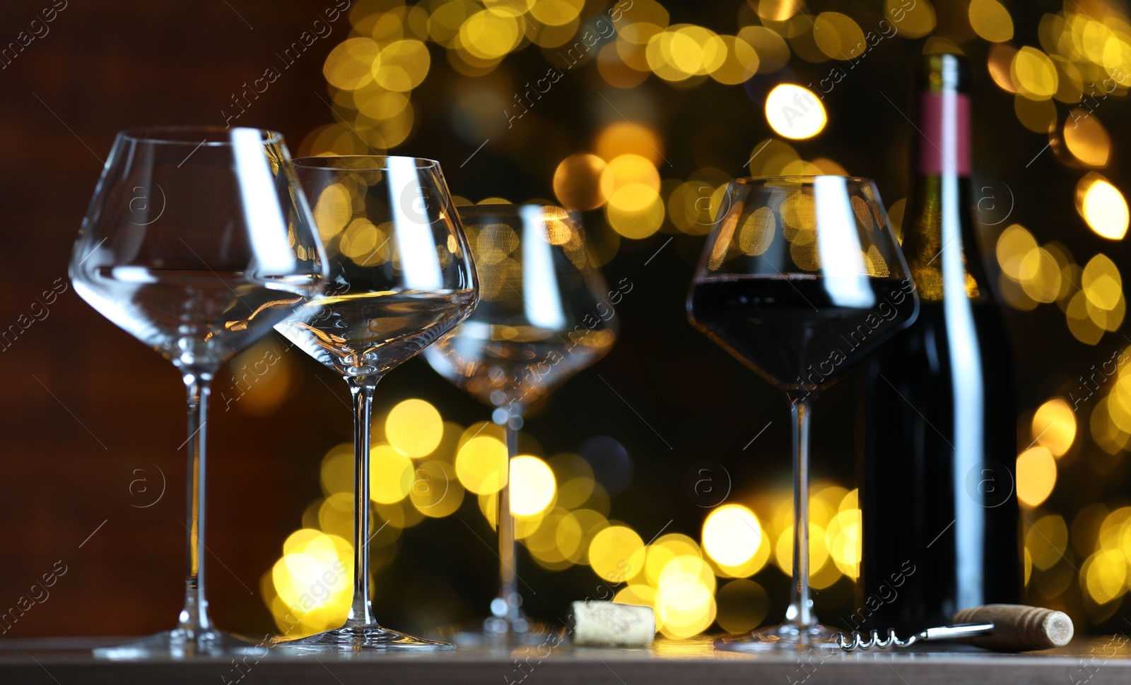 Photo of Glass with red wine and empty ones on table against blurred lights. Bokeh effect