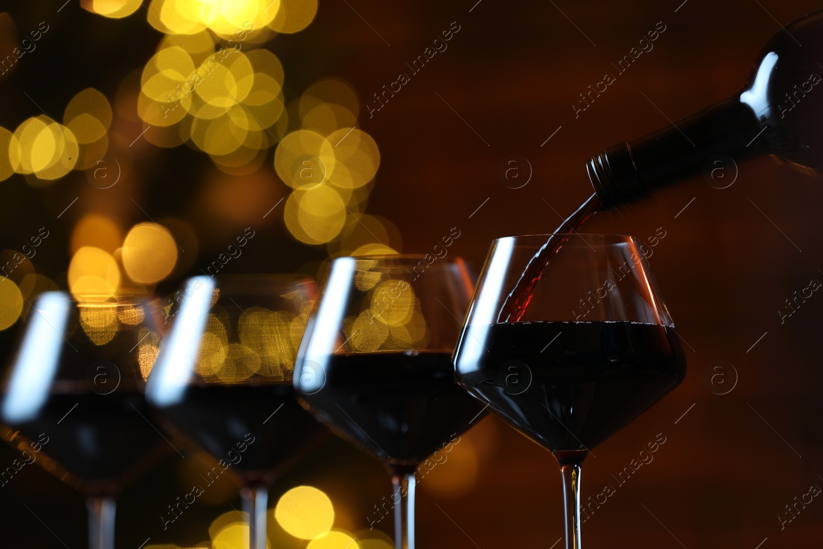 Photo of Pouring red wine into glass against blurred lights, closeup. Bokeh effect