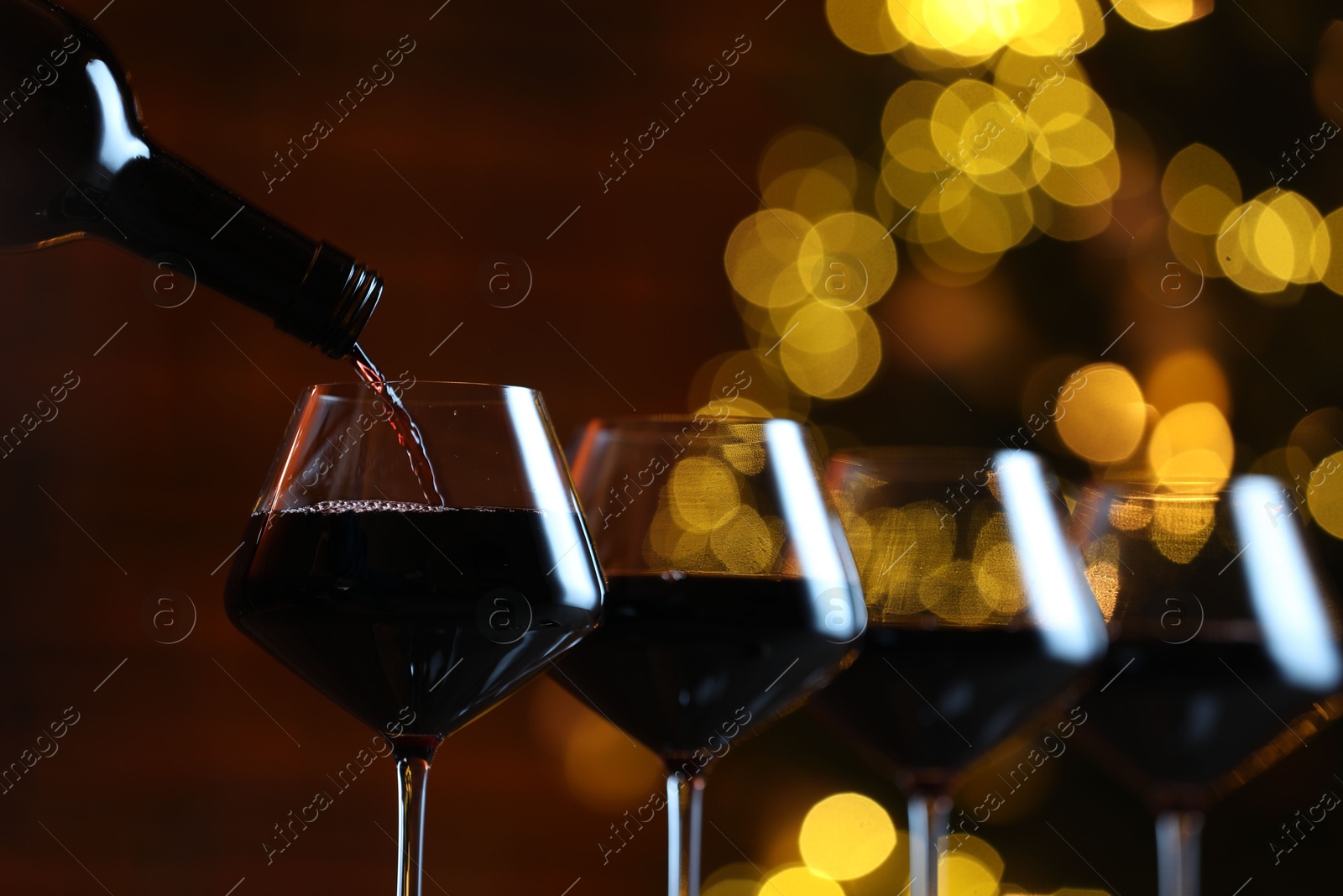 Photo of Pouring red wine into glass against blurred lights, closeup. Bokeh effect