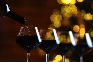 Photo of Pouring red wine into glass against blurred lights, closeup. Bokeh effect