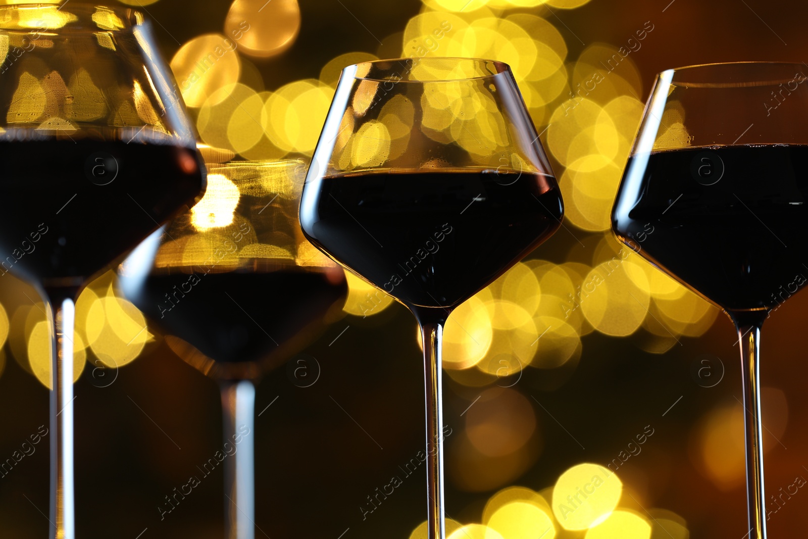 Photo of Tasty red wine in glasses against blurred lights, closeup. Bokeh effect