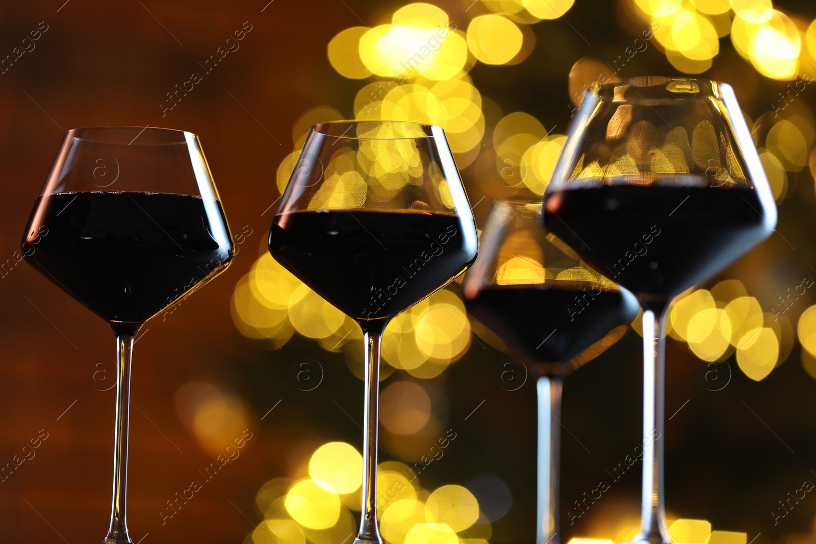 Photo of Tasty red wine in glasses against blurred lights, closeup. Bokeh effect