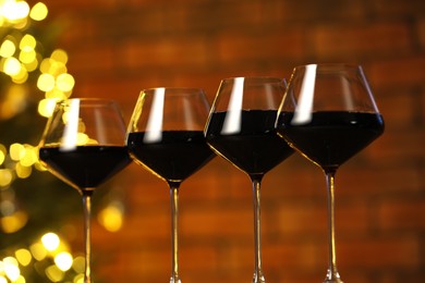 Photo of Tasty red wine in glasses against blurred lights, closeup. Bokeh effect