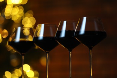 Photo of Tasty red wine in glasses against blurred lights, closeup. Bokeh effect