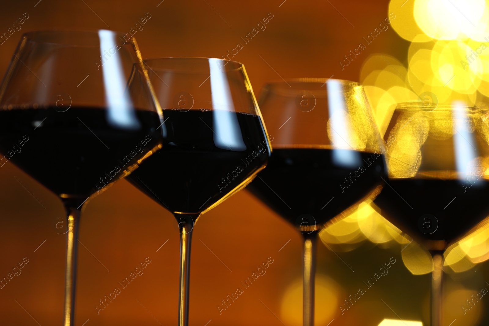 Photo of Tasty red wine in glasses against blurred lights, closeup. Bokeh effect