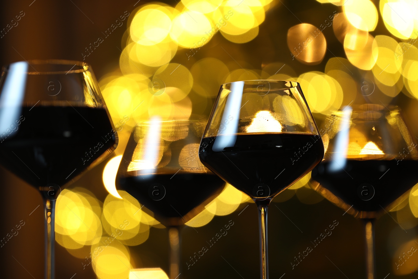 Photo of Tasty red wine in glasses against blurred lights, closeup. Bokeh effect