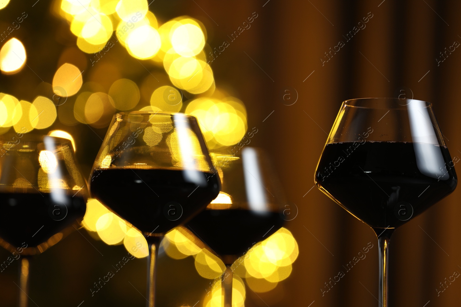 Photo of Tasty red wine in glasses against blurred lights, closeup. Bokeh effect