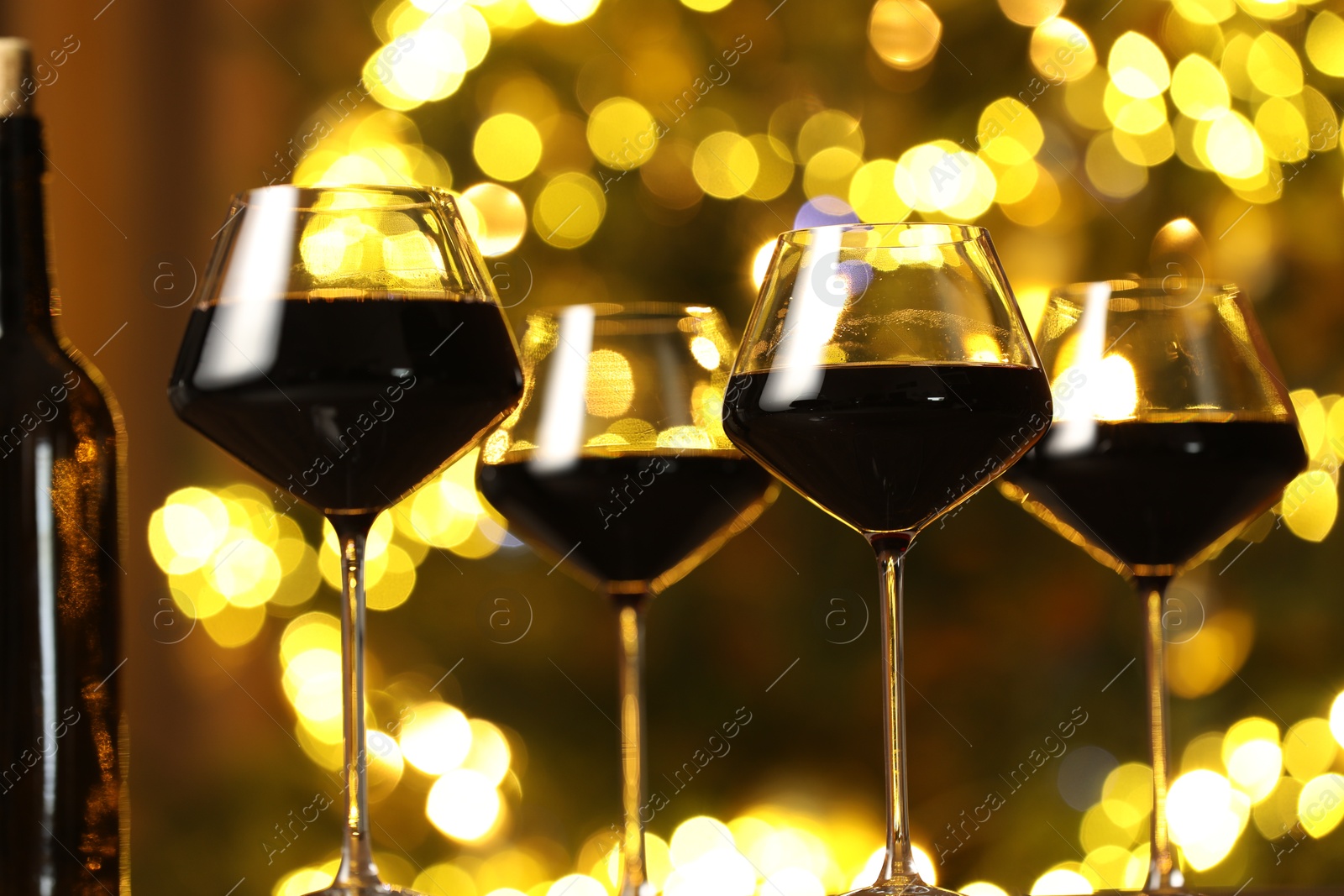 Photo of Tasty red wine in glasses against blurred lights, closeup. Bokeh effect