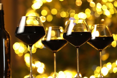 Tasty red wine in glasses against blurred lights, closeup. Bokeh effect