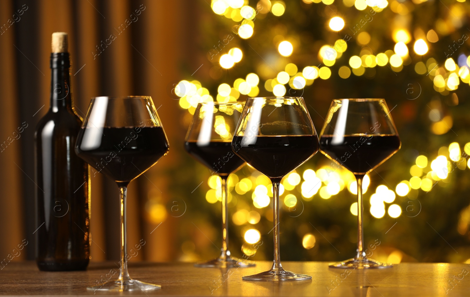 Photo of Tasty red wine in glasses on table against blurred lights. Bokeh effect