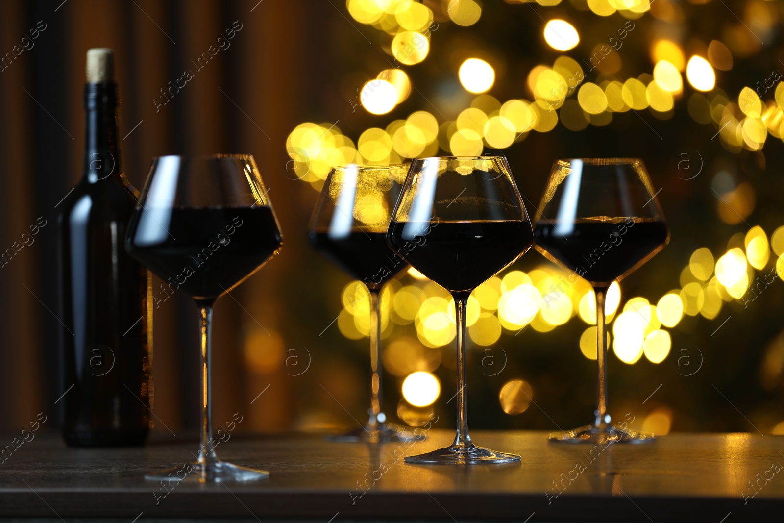 Photo of Tasty red wine in glasses on table against blurred lights. Bokeh effect