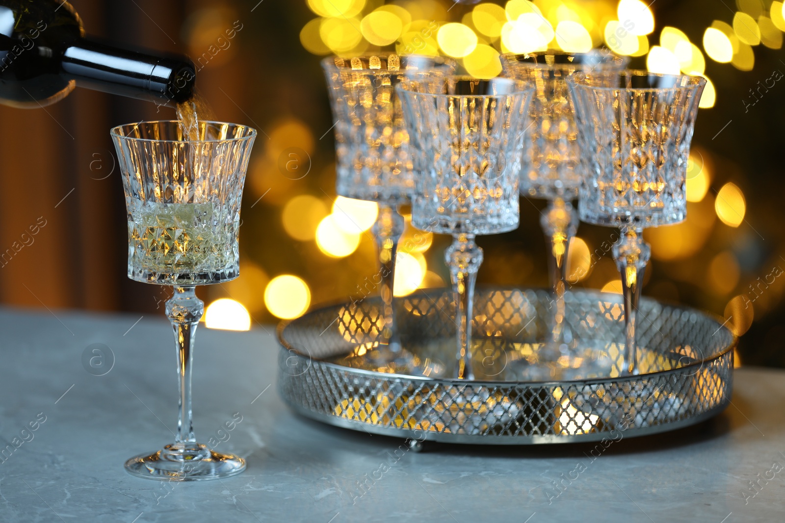 Photo of Pouring white wine into glass on table against blurred lights, closeup. Bokeh effect