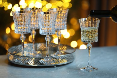 Photo of Pouring white wine into glass on table against blurred lights, closeup. Bokeh effect