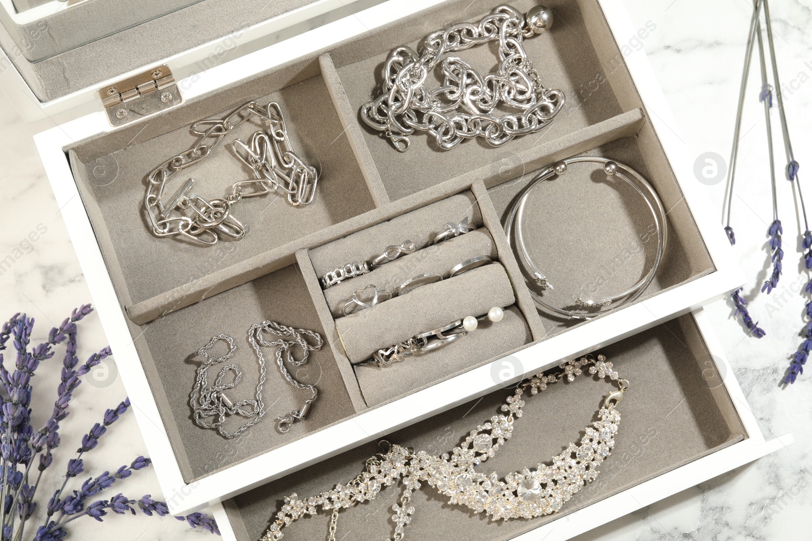 Photo of Many beautiful accessories in jewelry box and lavender on white marble table, flat lay