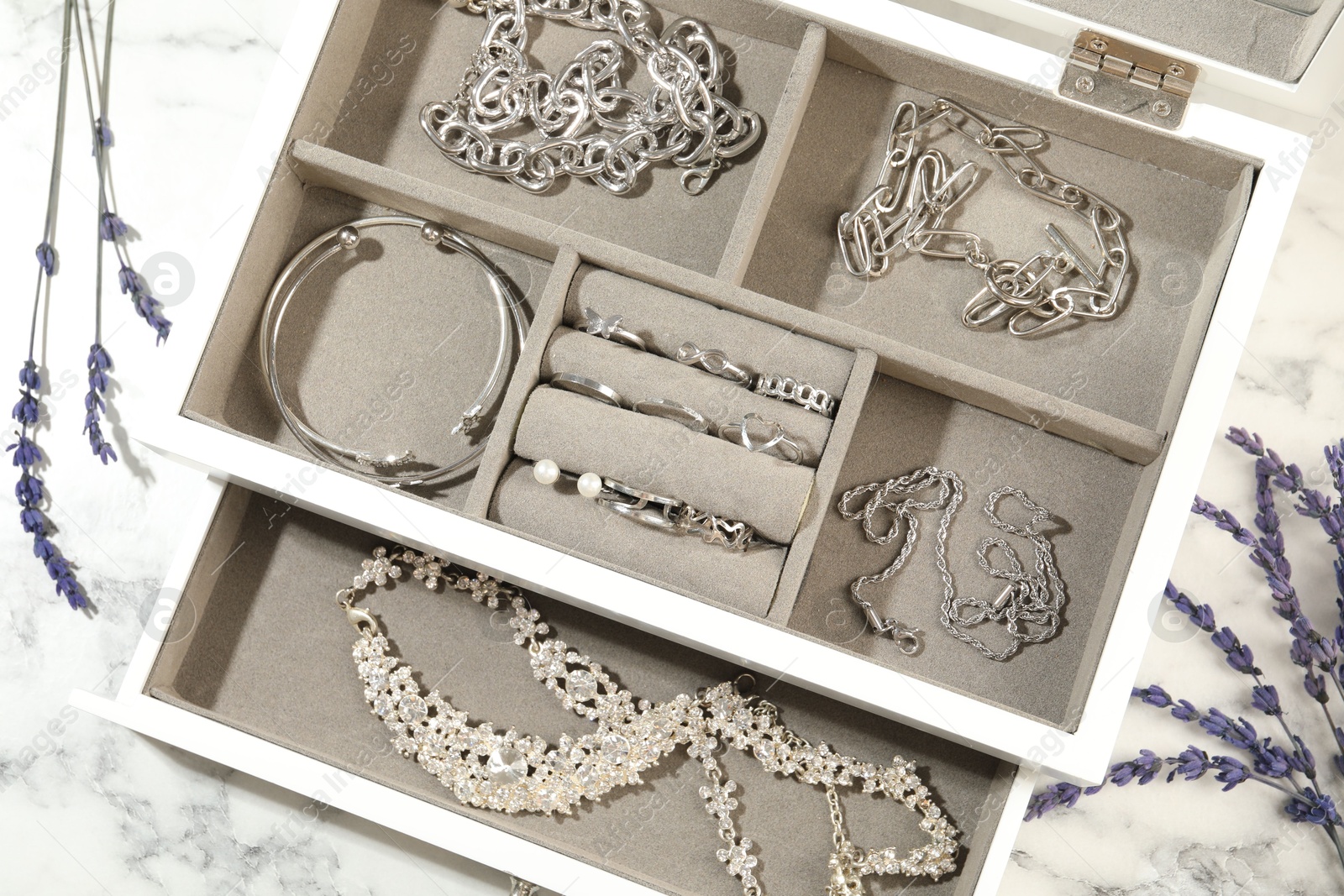 Photo of Many beautiful accessories in jewelry box and lavender on white marble table, flat lay