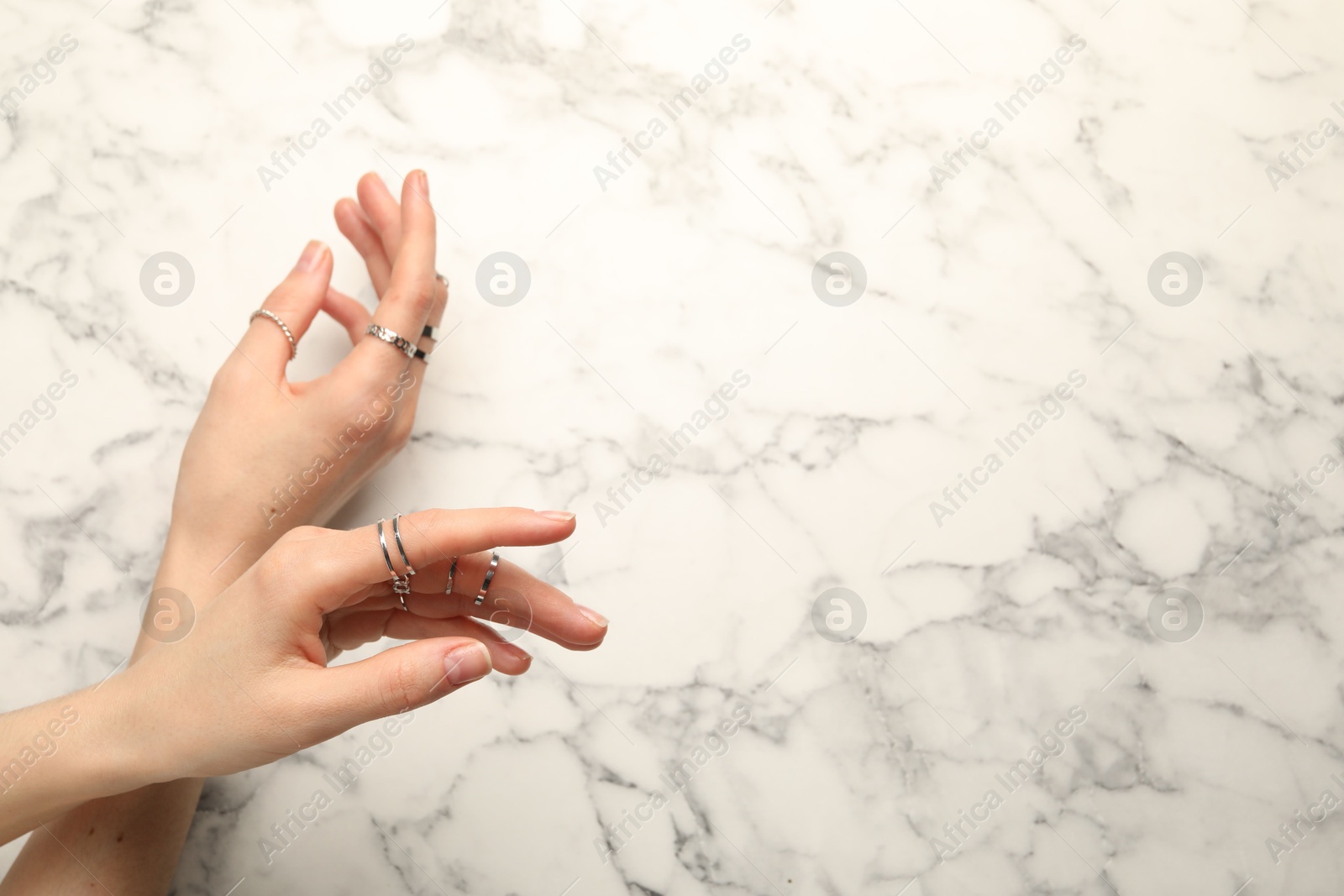 Photo of Woman wearing beautiful rings at white marble table, top view. Space for text